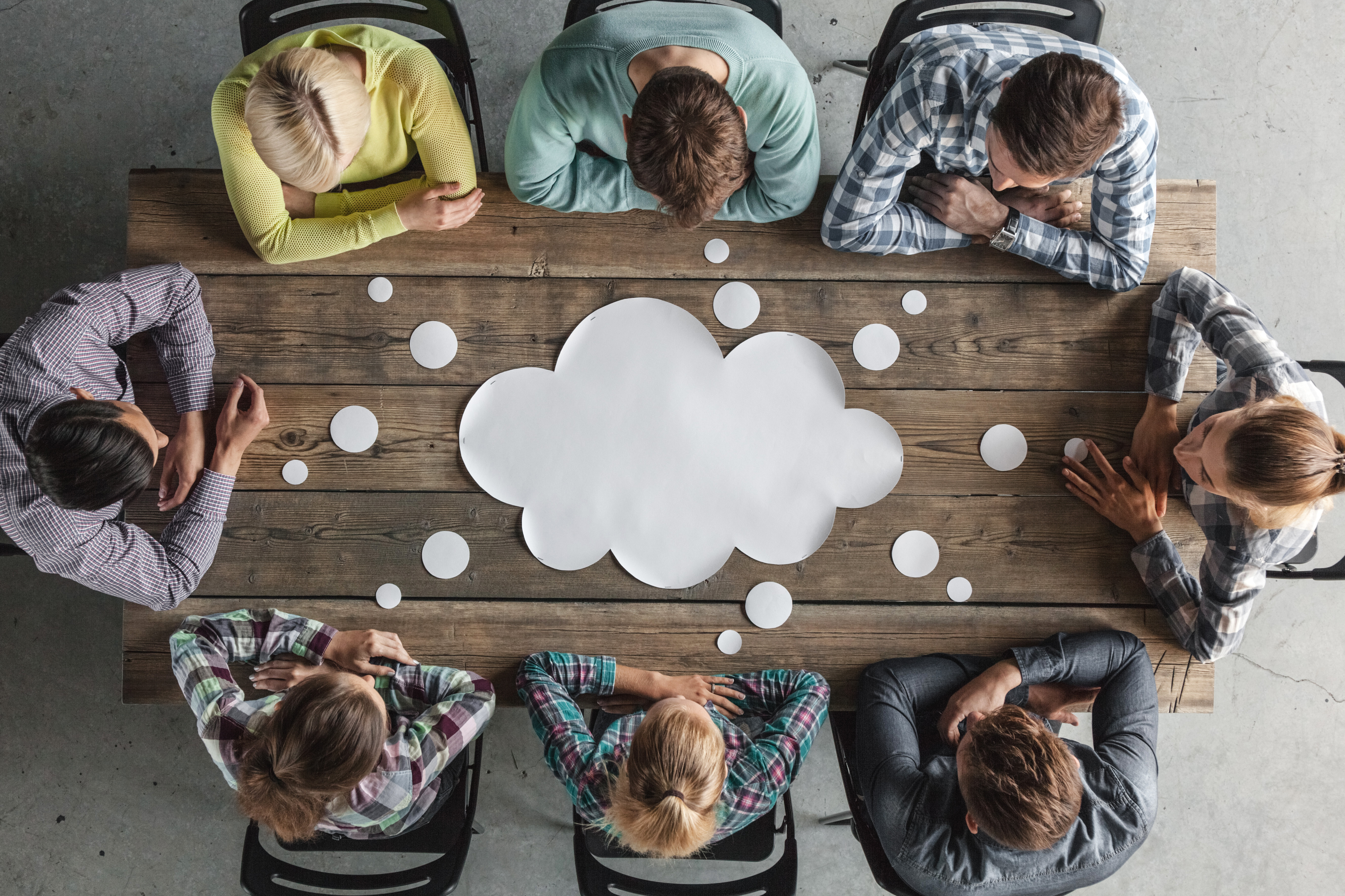 An above shot of a group of people around a desk with a paper cloud on the desk